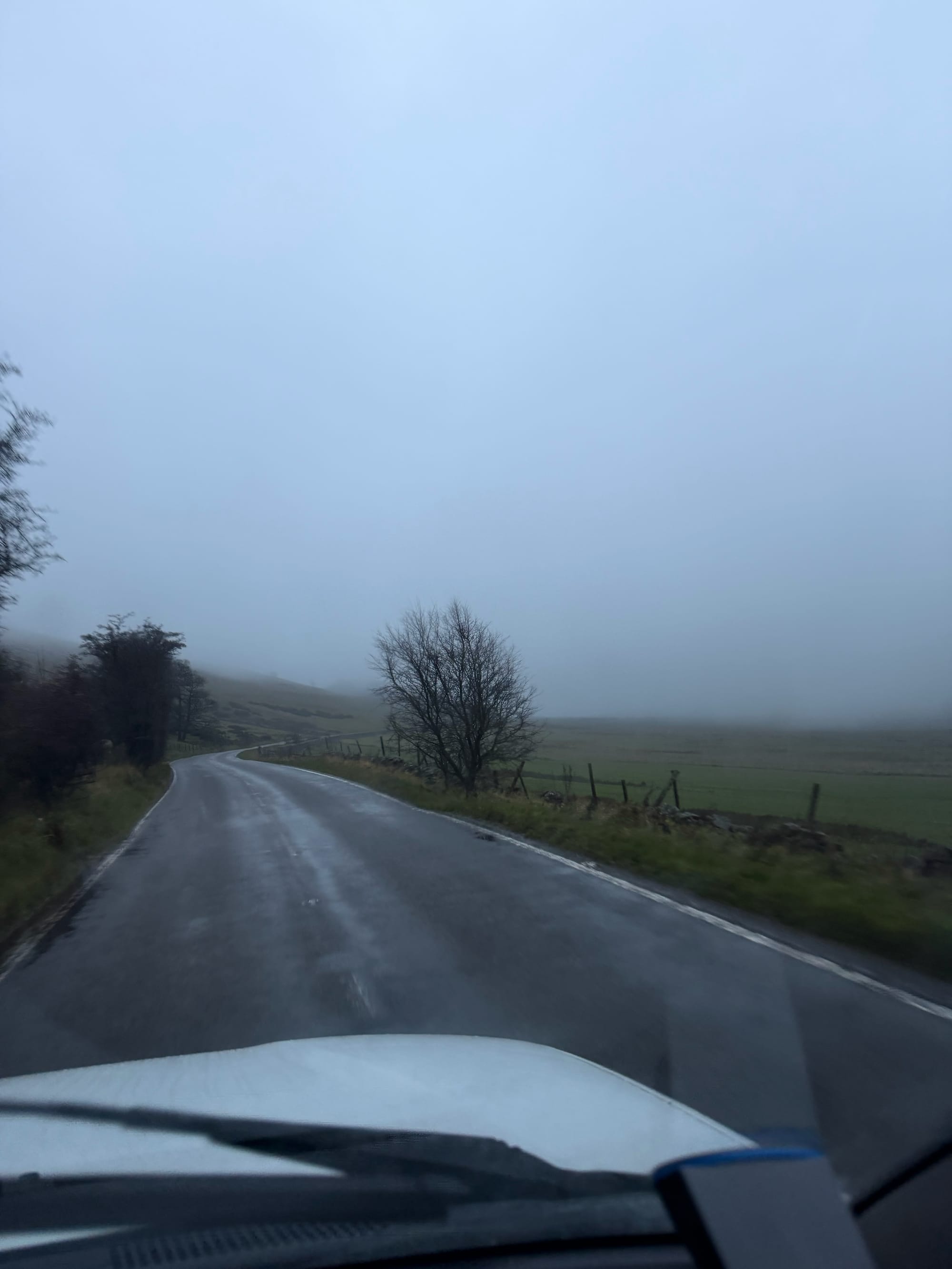 A car drives down a road. Mist is all around. 